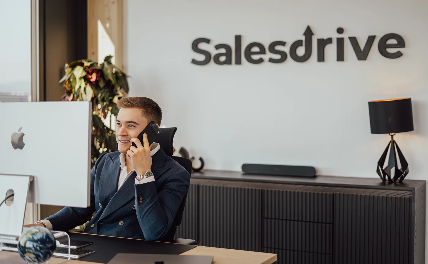 Lukas Lehner telefoniert an seinem Schreibtisch vor der SalesDrive-Logowand