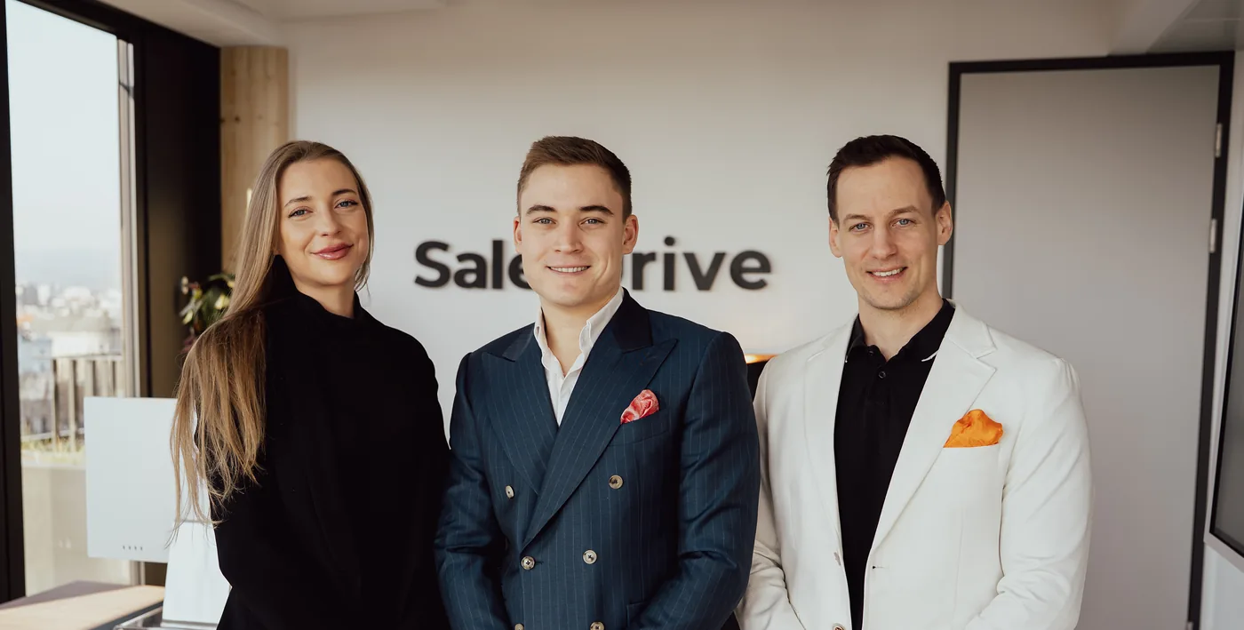 Eine Kollegin, Lukas Lehner und Alexander Kiraly vor der SalesDrive-Logowand im Büro in Wien